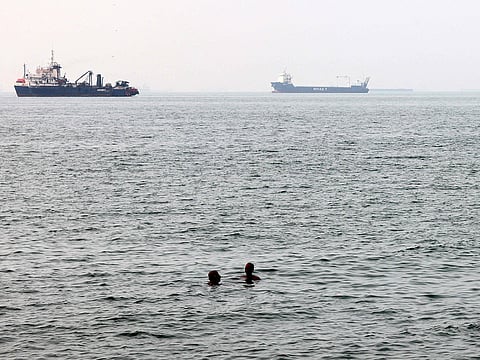 Men bathe in the Gulf waters as vessels in the background transit the Strait of Hormuz off the coast of Iran's southern port city of Bandar Abbas.