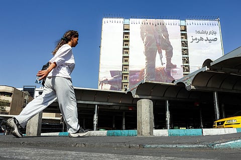 A woman walks near a giant billboard erected on the facade of a building depicting a member of Iran's Islamic Revolutionary Guards Corps (IRGC) placing his foot on a US sea drone, reportedly seized by Iran in the Strait of Hormuz.
