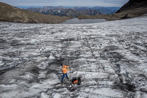 This aerial photograph shows glaciologist and head of 'Glacier Monitoring in Switzerland' (GLAMOS) network Matthias Huss posing with a four-metre-long measuring stake indicating the amount of ice that melted over the past year, during a measurement visit to record changes in Scex Rouge glacier, above Les Diablerets, western Switzerland, on September 24, 2026, ahead of the publication of the annual report on state of Swiss glaciers.