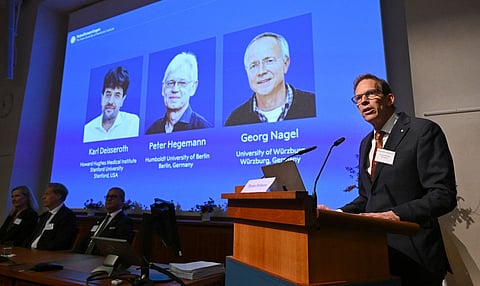 Nobel Committee Secretary General Thomas Perlmann ) speaks to the media in front of a screen displaying the names of this year's laureates (from left) Karl Deisseroth, Peter Hegemann and Georg Nagel during the announcement of the winners of the 2026 Nobel Prize in Physiology or Medicine at the Karolinska Institute in Stockholm, Sweden, on October 5, 2026.