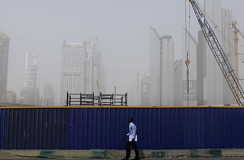 A man walks by a barrier during the hazy day in Dubai.
