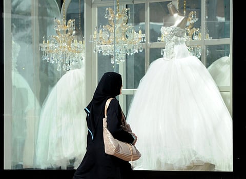 A Saudi woman walks past wedding dresses displayed in a shop window at a mall in Riyadh.