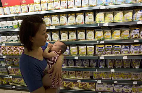 A woman carries a child past powdered milk products. Photo for illustrative purposes.