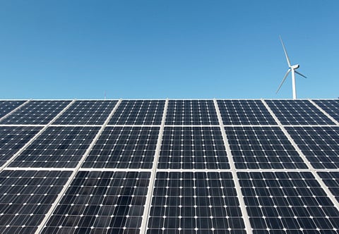 A wind turbine is seen over the panels of a solar power plant.
