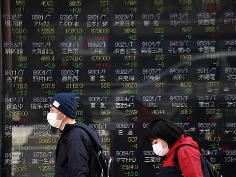 A man and a woman walk past an electronic stock at a securities firm in Tokyo. Asian markets rallied again on Thursday and oil prices built on the previous day's surge as investors began to see a glimmer of light at the end of the tunnel in the fight against coronavirus, following news of a possible breakthrough in the search for a treatment.