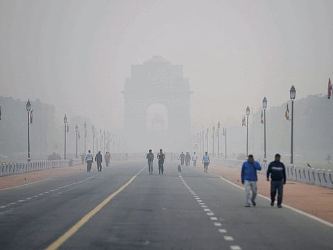 People walk early in the morning as smog covers India Gate war memorial in New Delhi.