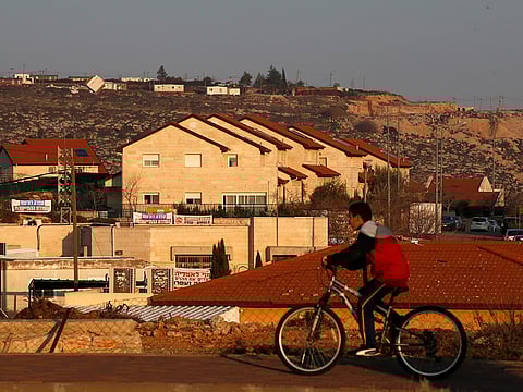 In this file picture, a boy rides his bicycle past houses in the Israeli colonies of Ofra, in the Occupied West Bank on February 6, 2017.