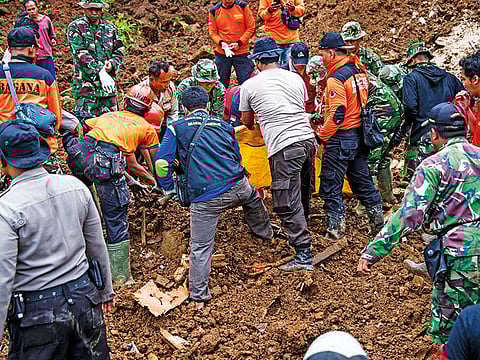 Indonesian rescuers recover the body of a woman from the scene after a wall of mud slammed onto houses from a hillside following heavy rainfall in Ponorogo district, East Java, yesterday. At least two people were killed and 26 are feared buried under heavy mud after a landslide struck Indonesia, the national disaster agency said.