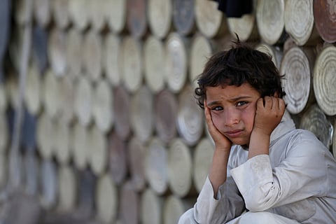 A boy sits next to a hut at a camp for the displaced by the Yemen war