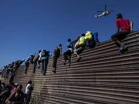 A group of Central American migrants climb a metal barrier on the Mexico-US border near El Chaparral border crossing, in Tijuana, Baja California State, Mexico, on November 25, 2018.