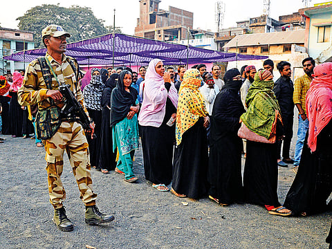 A soldier stands guard as women queue to cast their votes outside a polling station during the Madhya Pradesh assembly election in Jabalpur.