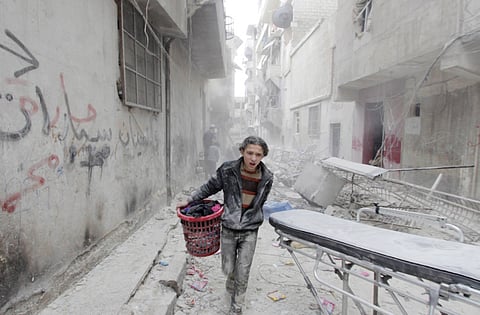 In this file photo, a boy carries his belongings at a site hit by a barrel bomb dropped by forces loyal to Syria's President Bashar Al Assad in Aleppo's Al Fardous district, Syria.