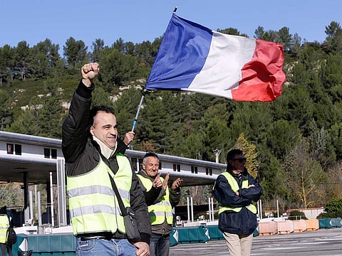 A demonstrators wearing a yellow vest clenches his fist as protesters open the toll gates on a motorway near Aix-en-Provence, southeastern France, Tuesday, December 4, 2018.