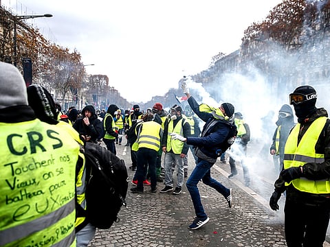 Protestors wearing "yellow vests" (gilets jaunes) send back tear gas canisters during clashes with riot police (unseen) during a protest against rising costs of living in the Champs Elysees in Paris