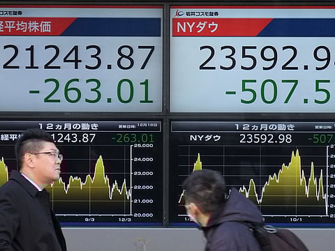 Pedestrians walk past a stock indicator board showing share prices of the Tokyo Stock Exchange (L) and the New York Dow (R) in Tokyo on December 18, 2018