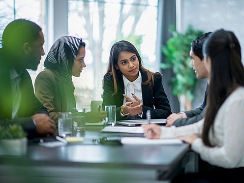 A multi-ethnic group of business people are indoors in an office boardroom.