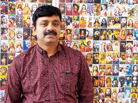 Lorence Maman Neriamparampil poses in front of the collection of unique pictures of Jesus.