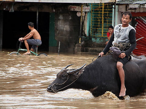 People wade through a flooded street in the town of Baao in Camarines Sur province on December 30, 2018. Four people were killed in landslides and thousands of others evacuated from their homes after a storm swept through the central Philippine islands on December 29, officials said.