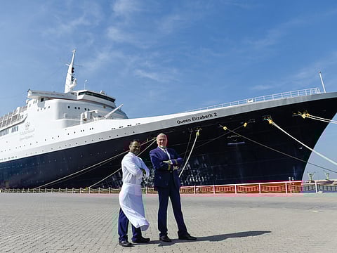 Ramasamy Pavadai (left) and Peter Warwick pose with the QE2, which is now a floating hotel docked at Port Rashid.