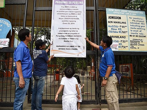 Children (C) look on as workers put up signage advising the public of the Manila Zoo's temporary closure, in Manila.