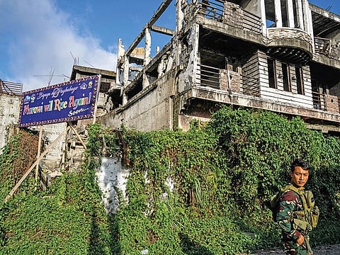 A billboard saying ‘Marawi will rise again! Soon ...’ stands against a backdrop of ruins from the siege in Marawi.