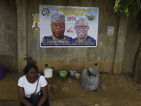 A woman sits beside a poster at the campaign headquarters of main opposition PDP party presidential candidate Atiku Abubakar (L) and his running mate for vice president Peter Obi following the cancellation of a campaign rally by the opposition Peoples Democratic Party (PDP) in Abuja, on February 9, 2019.