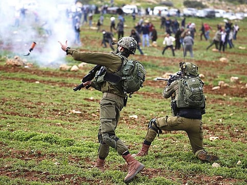 An Israeli soldier throws a tear gas canister at Palestinian demonstrators during a protest against Jewish settlements, in al-Mughayyir village near Ramallah