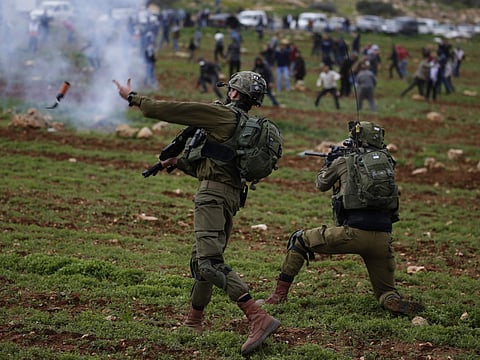 An Israeli soldier throws a tear gas canister at Palestinian demonstrators during a protest near Ramallah