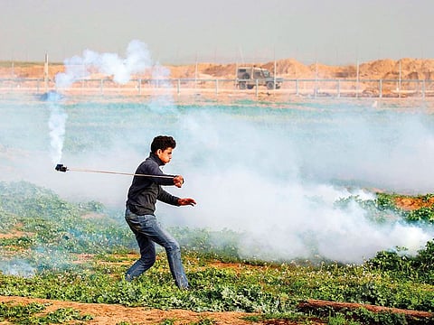 A Palestinian protester uses a slingshot to throw back a tear-gas canister at Israeli forces following a demonstration near the fence along the border with Israel east of Gaza City