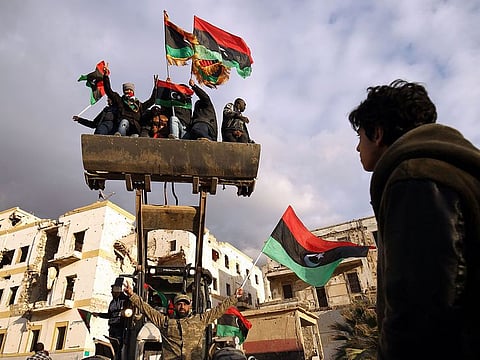 Libyan men on a bulldozer wave the national flag as they gather to mark the eighth anniversary of the uprising in Libya's second city of Benghazi