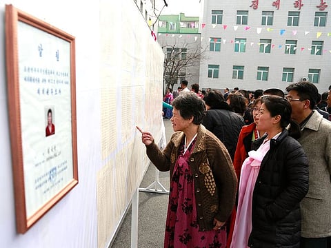 People inspect the list of voters as portrait of a candidate for the national legislature is displayed on the left, during the election at a polling station in Pyongyang, North Korea