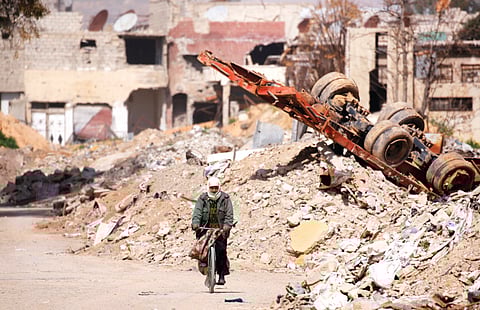 A man rides on a bike past rubble in Ein Terma, a district of eastern Ghouta, Syria