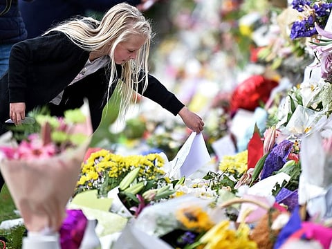 A young girl places a note among flowers left in tribute to victims in Christchurch