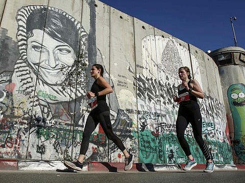 Athletes run past a barrier in the biblical town of Bethlehem in the occupied West Bank during the 7th International Palestine Marathon last year