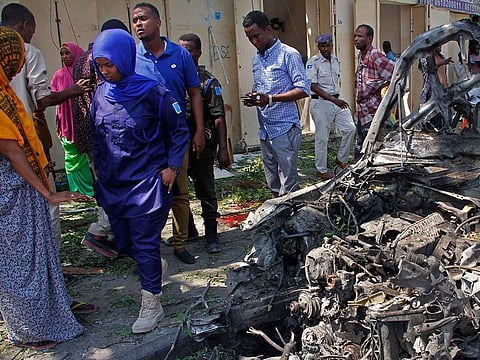 Police and civilians walk past a destroyed vehicle after an attack using an explosives-laden vehicle on a restaurant in Mogadishu, Somalia.