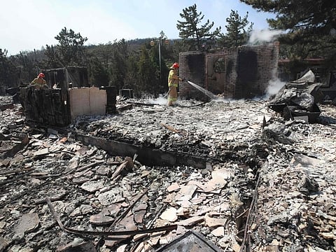 Firefighters spray water over the debris left after the area was hit by a forest fire in Donghae, Sout Korea, on Friday.