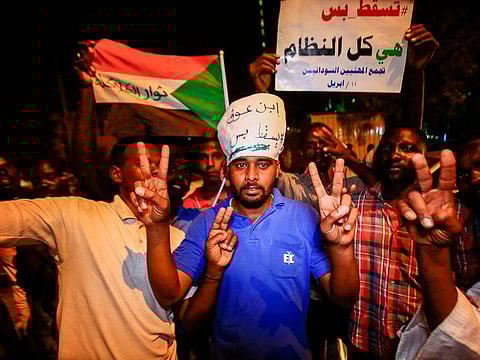 Sudanese protesters flash the victory gesture and raise a sign reading in Arabic "Just fall, that is all, the whole regime", during a demonstration against the new ruling military council put in place following the ouster of president Omar Al Bashir, in the capital Khartoum on April 11, 2019.