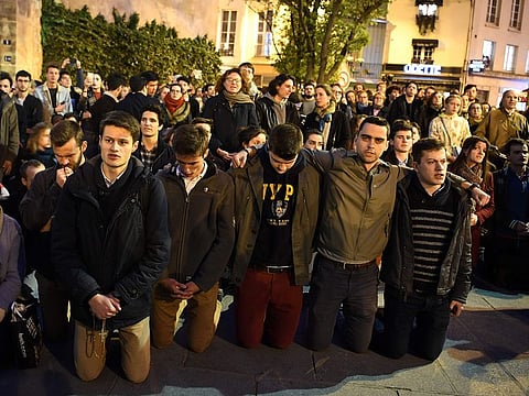 People kneel on the pavement as they pray outside watching flames engulf Notre-Dame Cathedral in Paris on April 15, 2019.