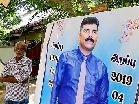 Velusami Raju, father of the Zion Church suicide blast victim Ramesh Raju, looks on next to a banner displaying Raju Ramesh's portrait at his house, in Kattankudy.