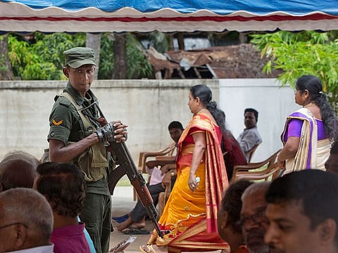 A soldier stands guard amid Catholics attending Mass outside St. Joseph's church in Thannamunai, Sri Lanka, on Tuesday, April 30, 2019.