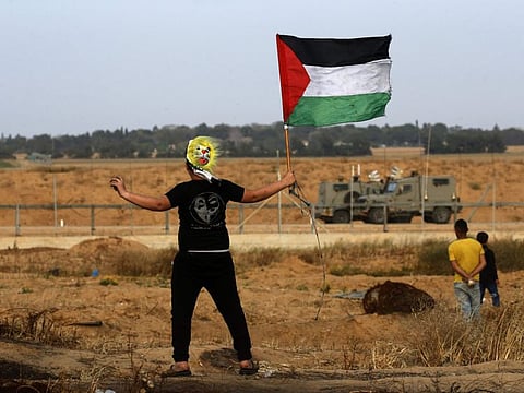 A Palestinian protester wearing a mask waves a national flag during a demonstration near the border with Israel, east of Khan Yunis in the southern Gaza Strip, on April 26, 2019.