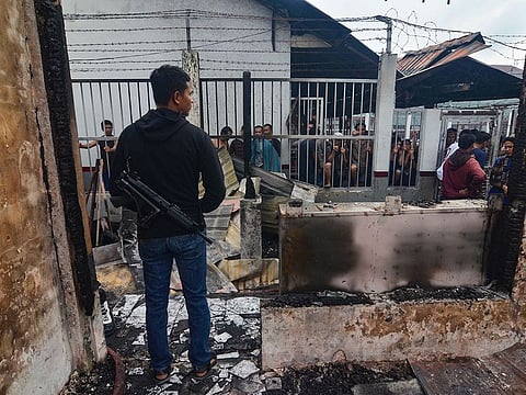 An armed plainclothes policeman (L) secures the around around Siak prison in Siak Sri Indrapura in Riau province on May 11, 2019 after rioting and a fire broke out at the detention centre leading to a prison break.
