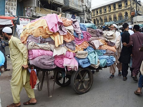 A worker pushes a cart carrying garments on a street in Karachi on Friday, May 10, 2019.