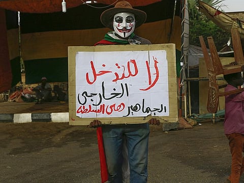 A Sudanese protester wearing a Guy Fawkes mask holds a placard with the slogan that reads in Arabic: "No for foreign intervention".