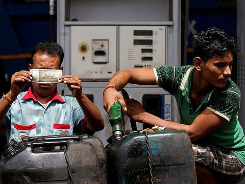 A worker checks a 500 Indian rupee note as a man fills diesel in containers at a fuel station in Kolkata, India