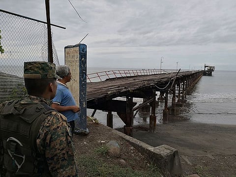 A police officer and resident look out at an abandoned pier after an earthquake made the office structure at the end incline to the right, in Puerto Armuelles, Sunday, May 12, 2019.