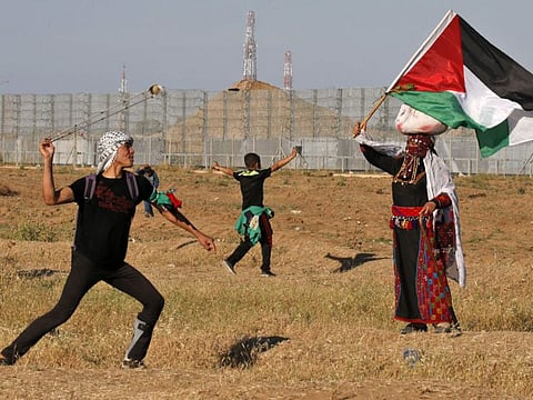 A protester hurls stones at Israeli troops as a woman wearing a traditional Palestinian outfit waves a national flag, during a demonstration near the border with Israel, east of Gaza City, on May 10, 2019.
