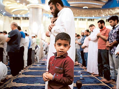 A boy looks on as Kuwaitis pray at the Sunni Grand Mosque in Kuwait City early yesterday. Kuwait has banned Eid prayers in open spaces this year and they will be confined to large mosques.