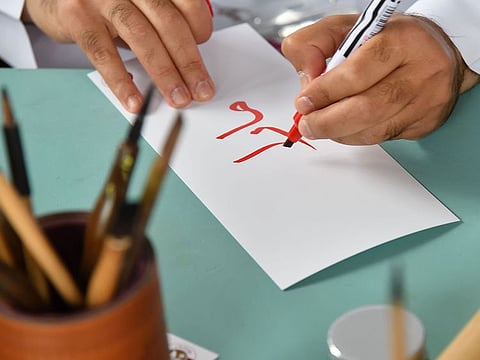 A man writing red arabic letters on a white sheet of paper. For illustrative purposes only.