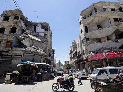 A man rides on a motorbike with his family past damaged buildings in the city of Idlib, Syria.